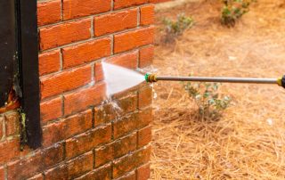 A pressure washer hose sprays dirt and grime off of a brick building.