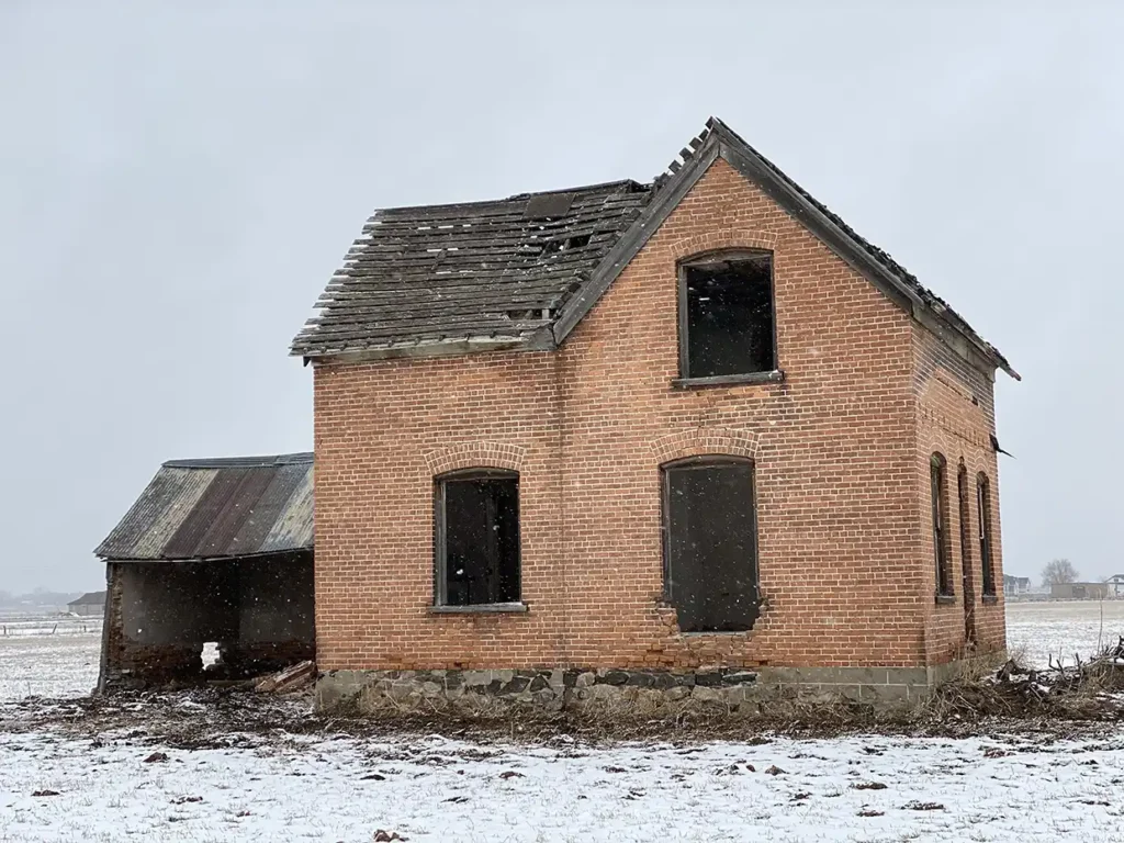 A small brick dwelling with missing windows and dilapidated roof